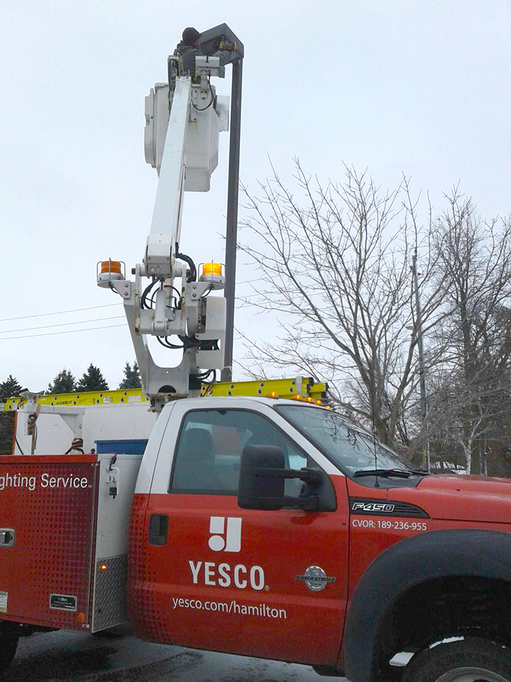 red Yesco service truck with the bucket ladder up fixing a pole light in a parking lot